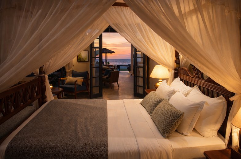 Ocean Courtyard Suite at IF Villa — canopy bed opening through French doors to a private patio and the sea
