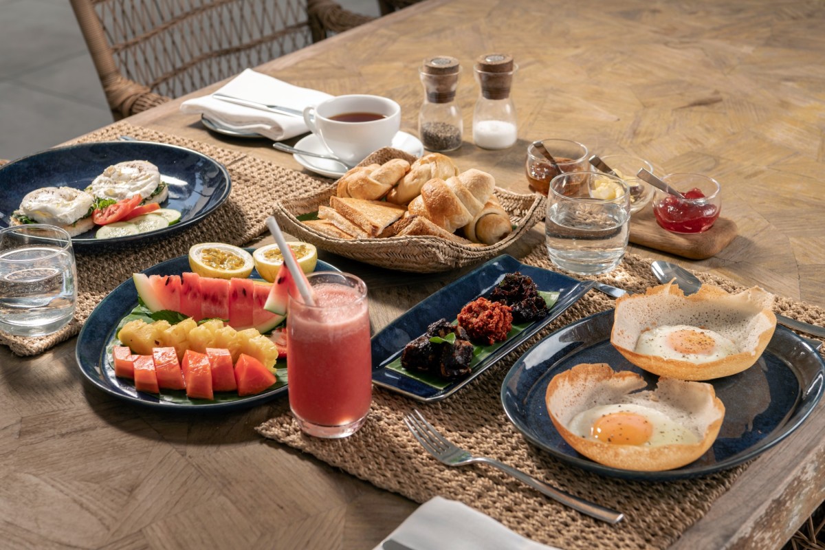 Breakfast spread with egg hoppers, tropical fruit, pastries and tea on a wooden table