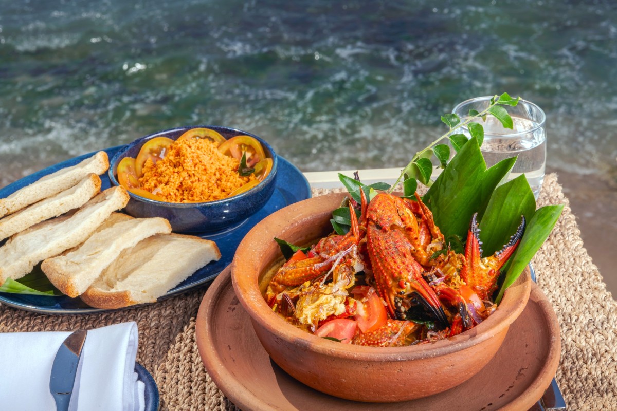 Clay pot of crab curry with pol sambol and bread, served at a table by the ocean