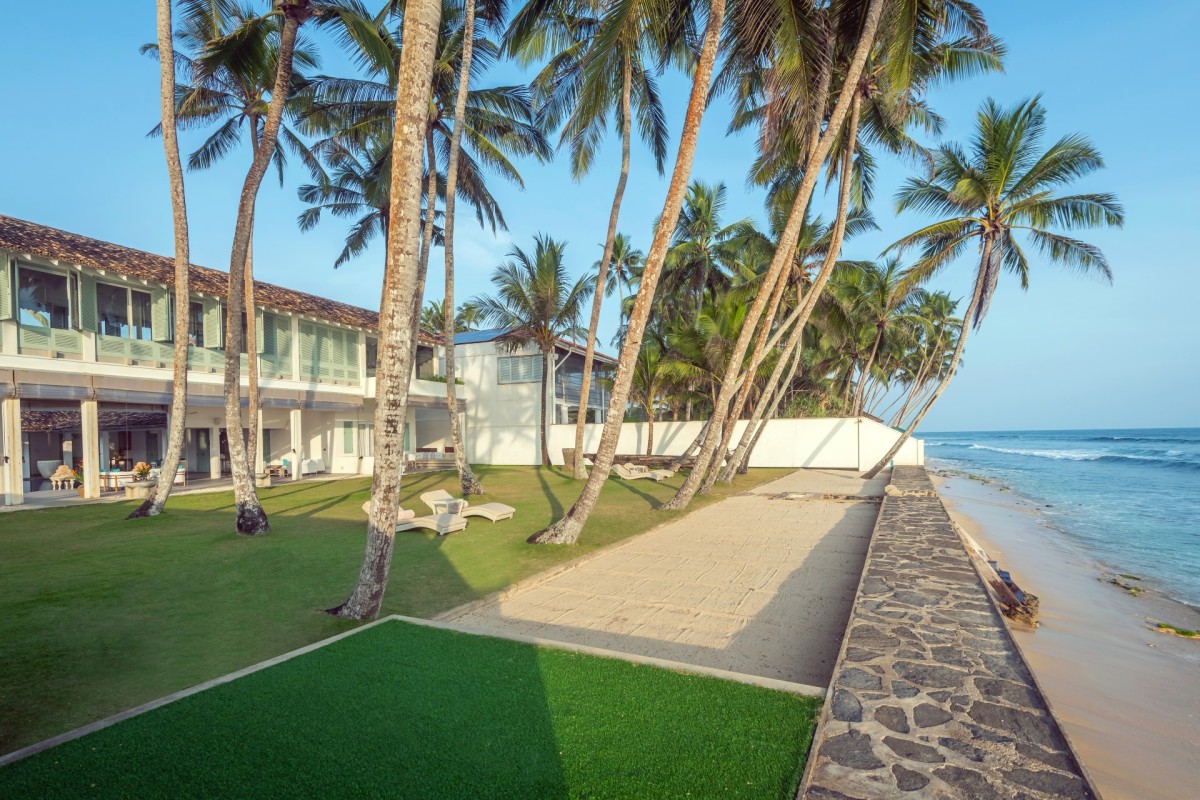 Palm lawn running from the villa down to the stone seawall and sandy beach
