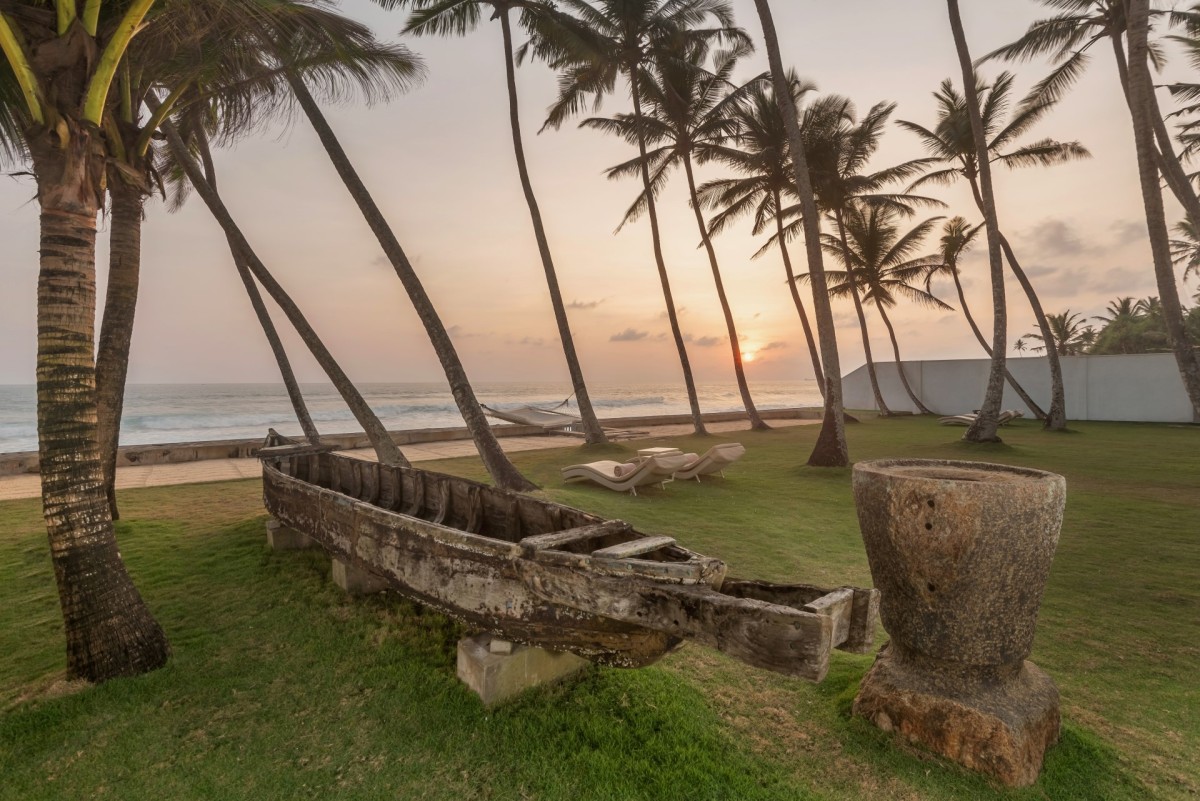 Sunset over the palm lawn with a traditional wooden boat and the ocean beyond