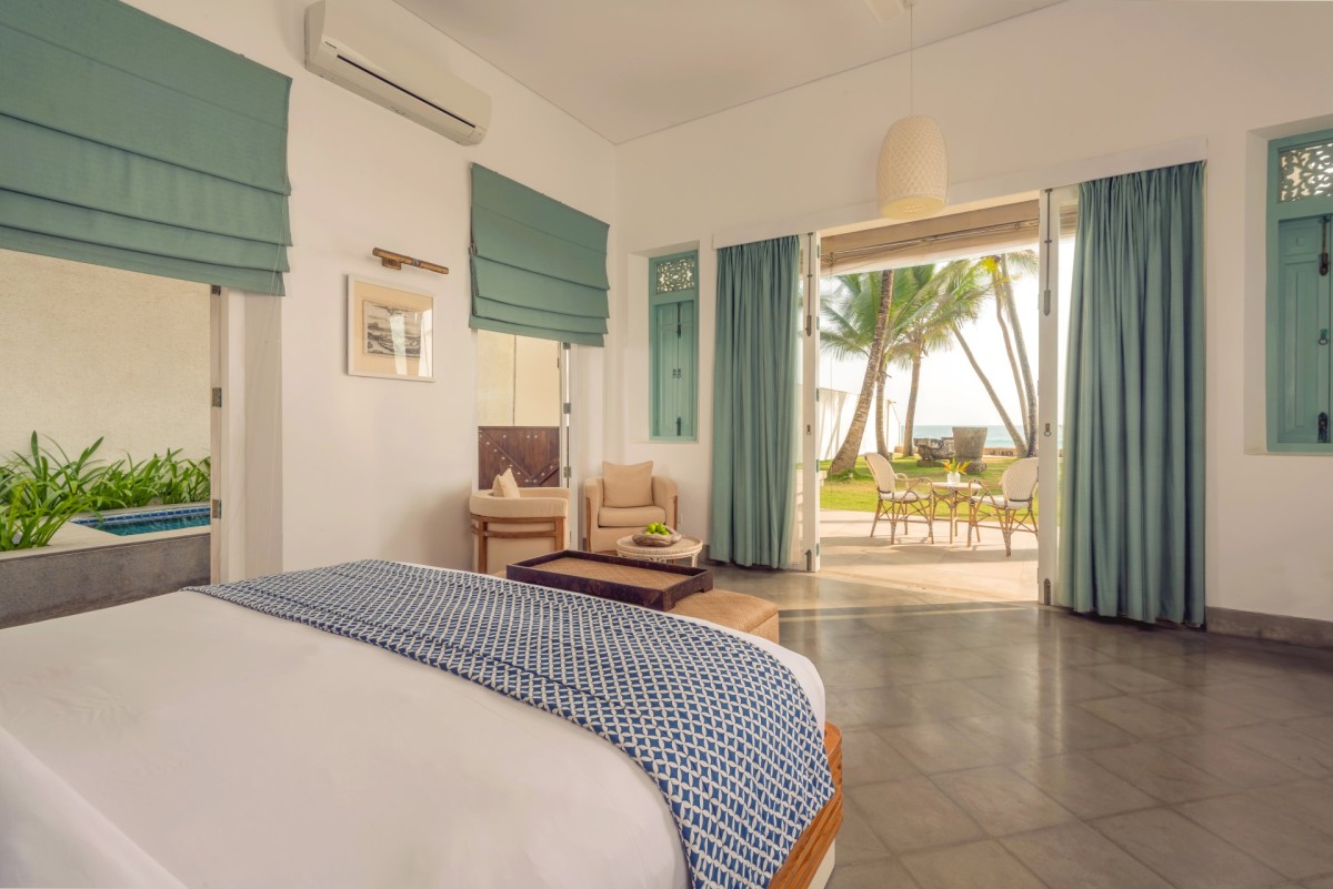 King bedroom at Ishq Talpe opening through glass doors to a garden patio, palms and the ocean
