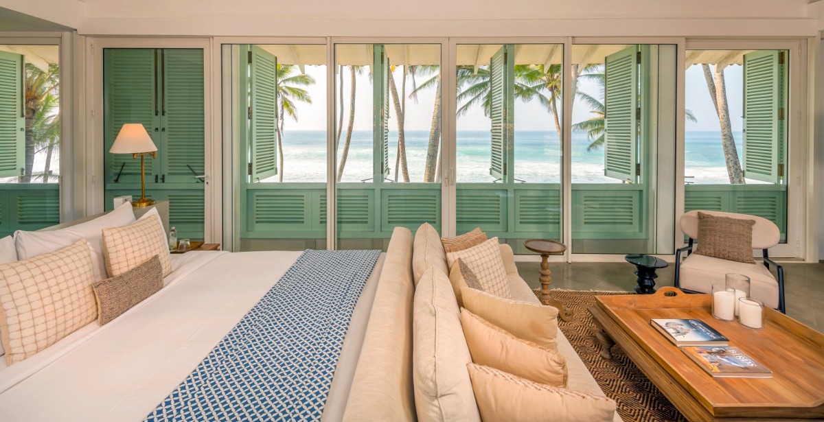Bedroom 4 at Ishq Talpe — a king bed and lounge chairs behind a wall of glass doors opening to the ocean