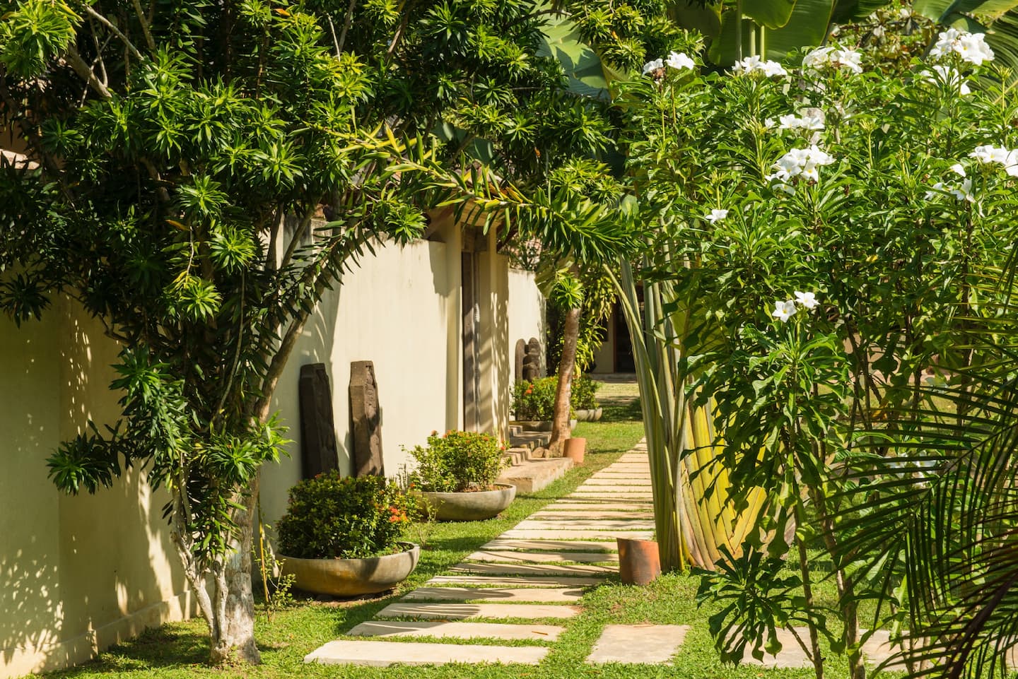 Stone garden path alongside Kumara Luxury Villa beneath tropical trees