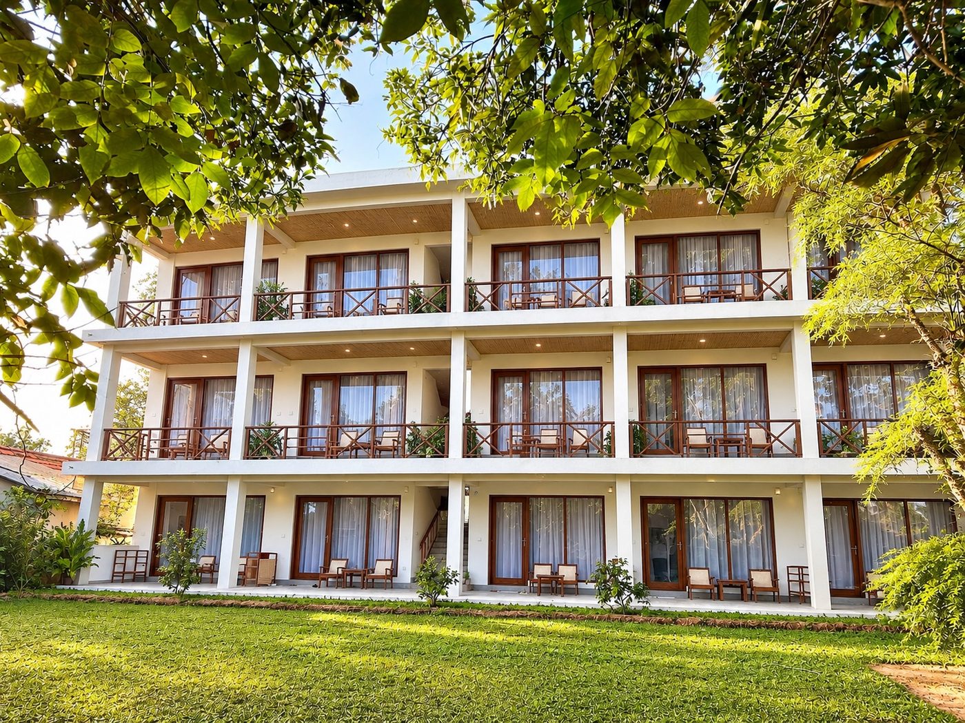 The Lily Mirissa hotel building seen from the garden lawn, framed by tall tropical trees