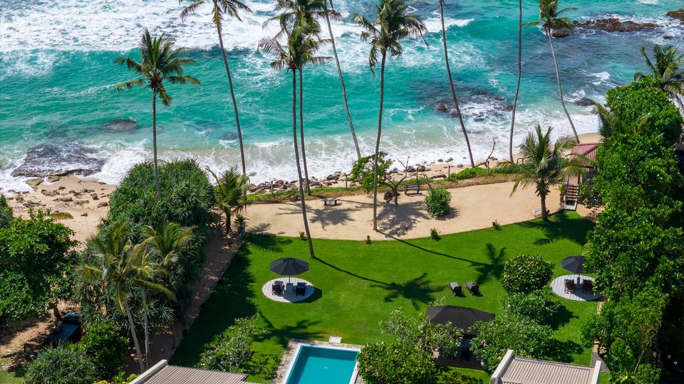 Aerial view of the Mirissa coastline and the villa's green grounds running down to the beach