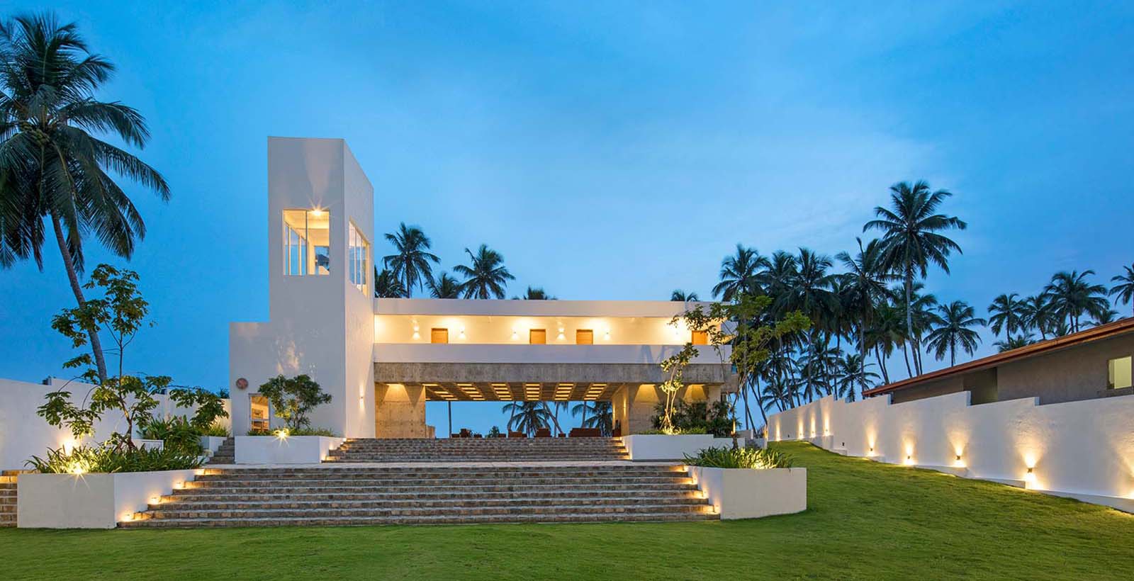Serendivi Resort Villa's white facade and entrance steps at dusk, framed by coconut palms