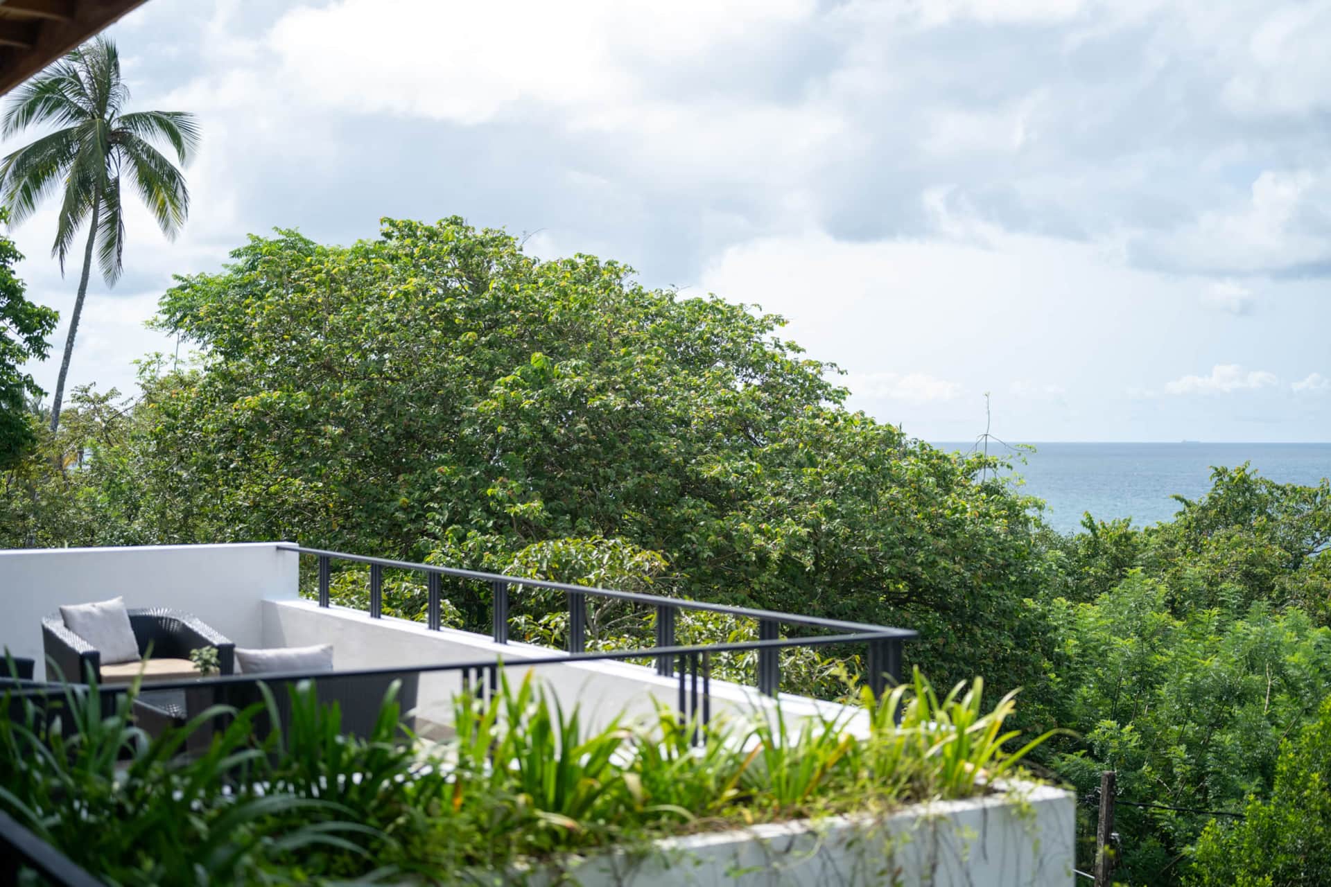 Rooftop seating area with jungle greenery and a glimpse of the ocean