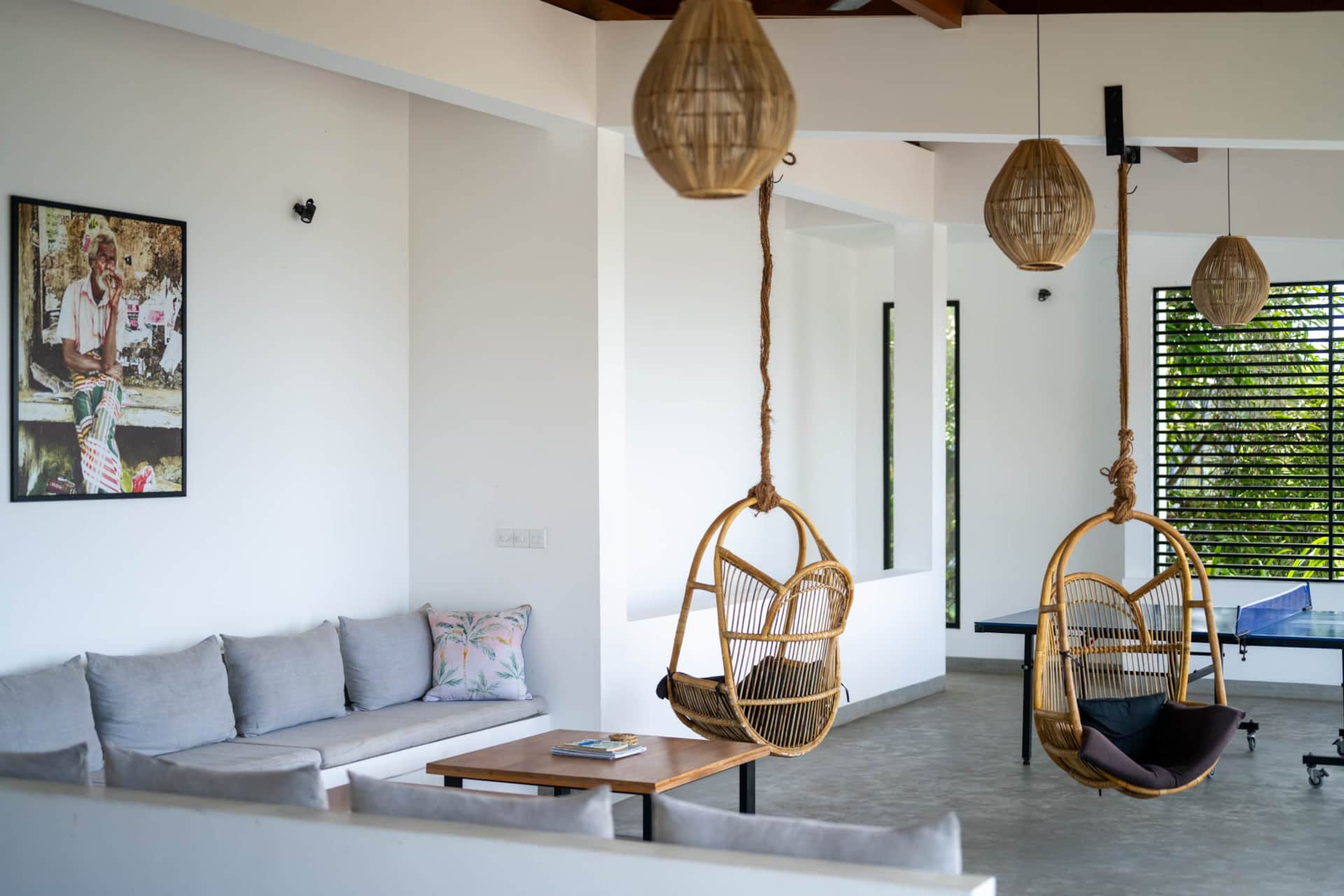 Living area with hanging rattan chairs, a sofa and a ping pong table