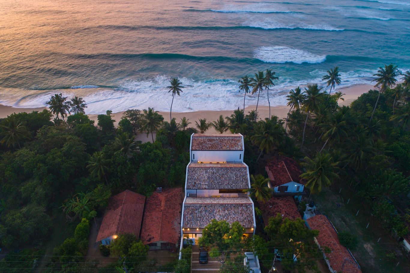 Aerial view of Three Gables Boutique Villa at sunset, showing its three tiled gables, palm trees and the surf on the private beach
